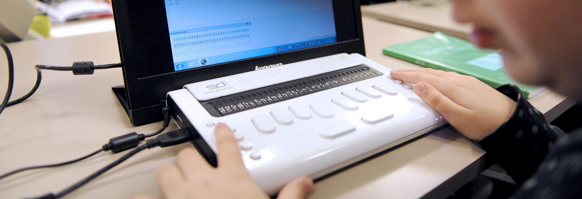 Un enfant sur un ordinateur avec sa ligne de braille informatisée